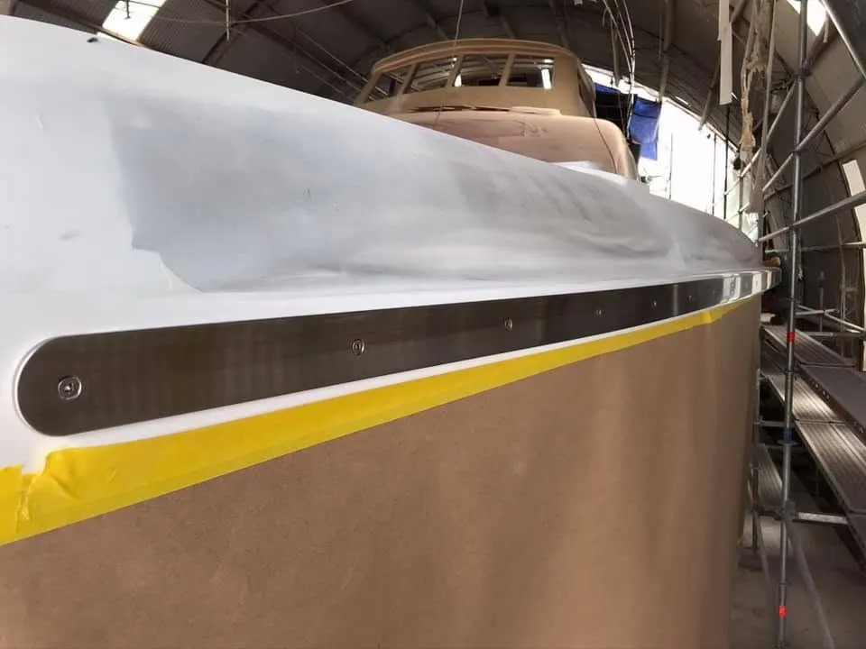 Boat hull with a masked yellow stripe inside a workshop.