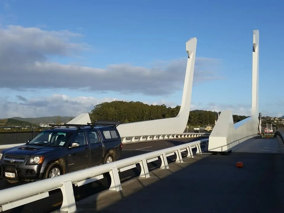 Roadside barrier and bridge structure beside a parked vehicle.