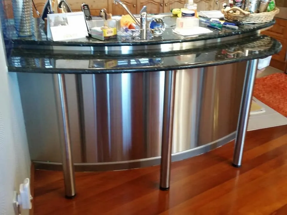 Curved stainless steel counter with a dark benchtop and tubular legs.