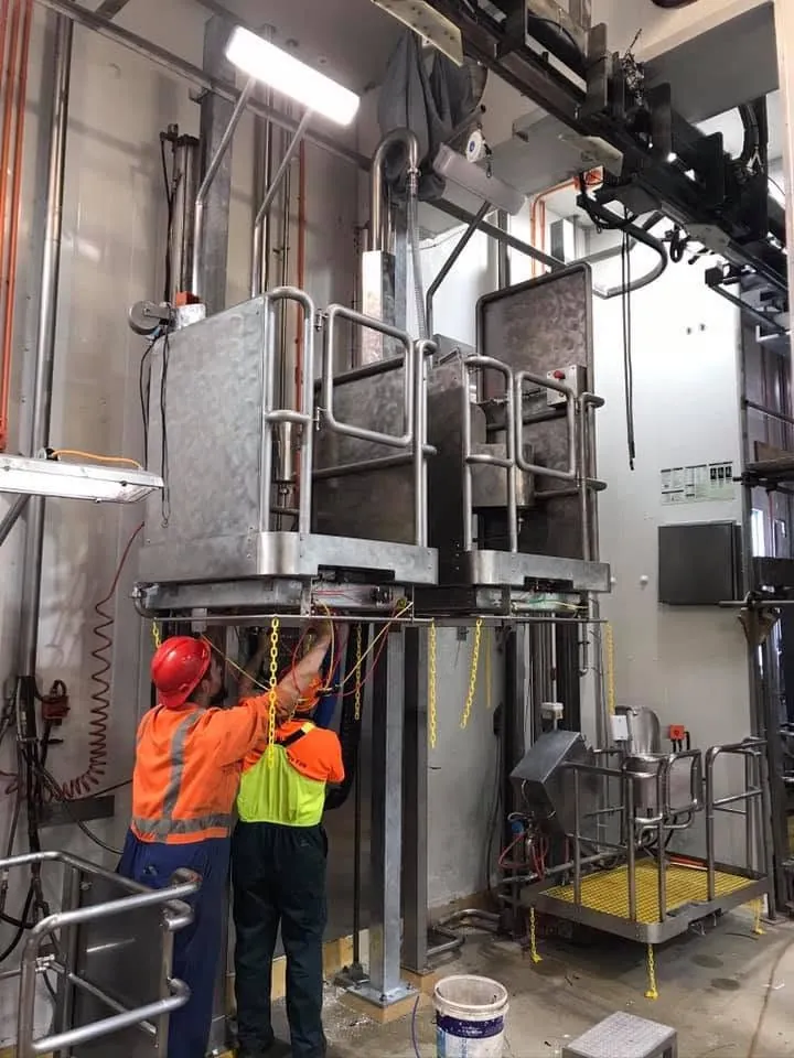 Workers in high-visibility clothing beside tall industrial equipment.