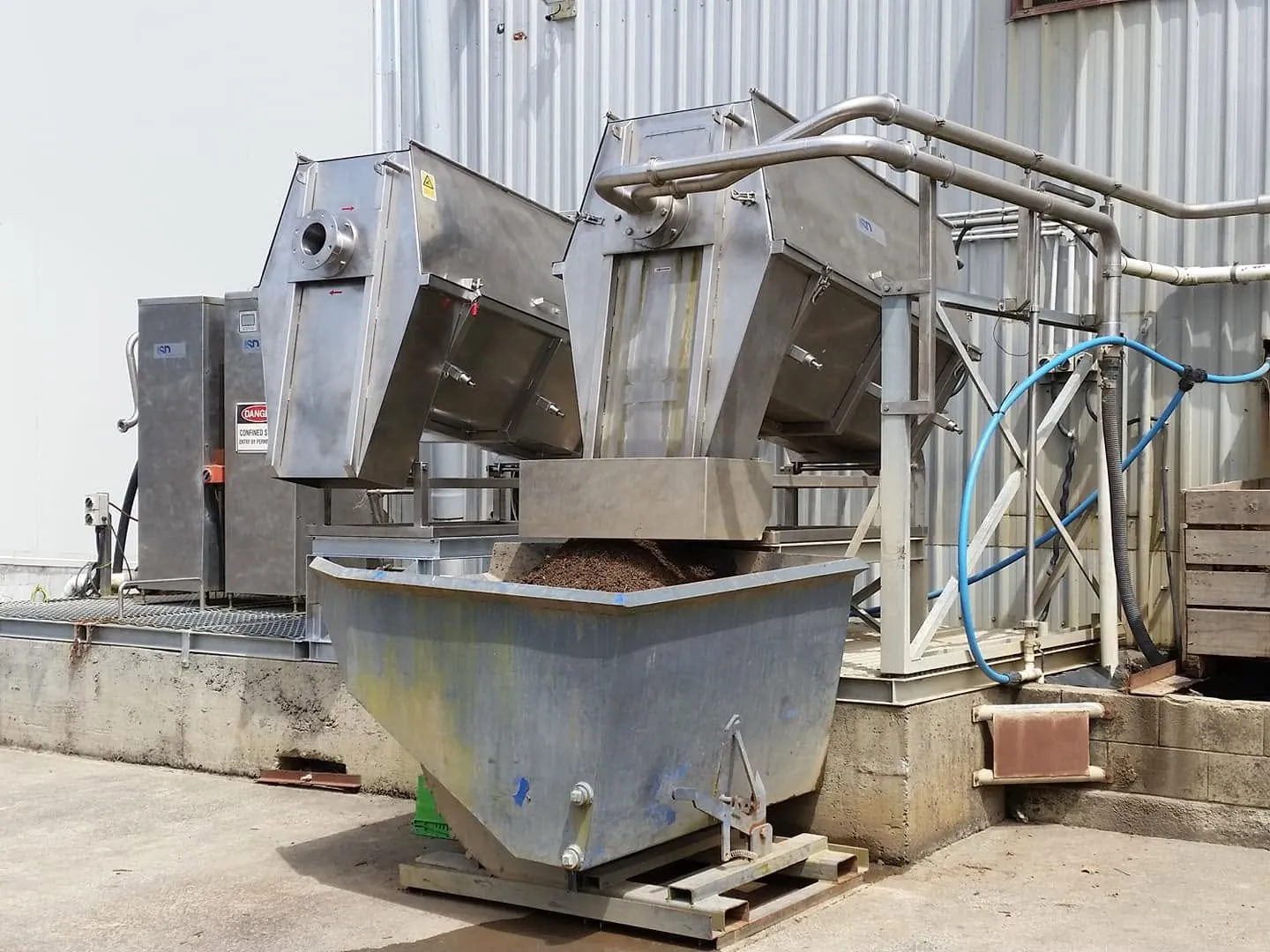 Stainless steel equipment with angular hoppers, pipework and a collection bin.